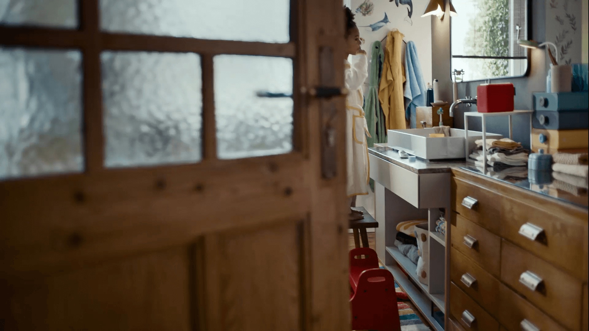 Still from the Tonies commercial – a child in a bathrobe at the bathroom sink, seen through a half-open wooden door 