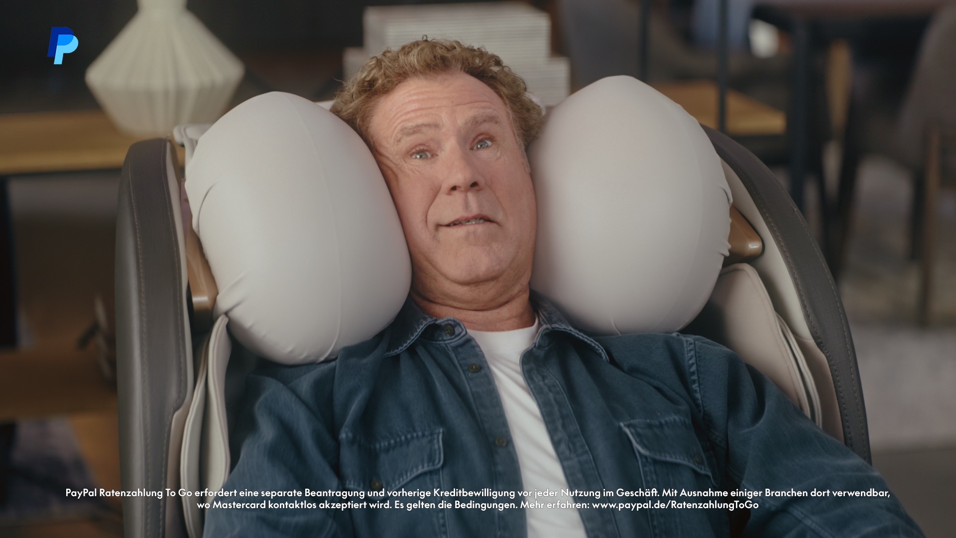 Still from the PayPal commercial – man reclining in a massage chair in a furniture showroom 